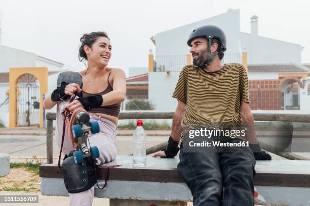 cheerful woman with roller skates looking at man while sitting on bench - inline skate bildbanksfoton och bilder