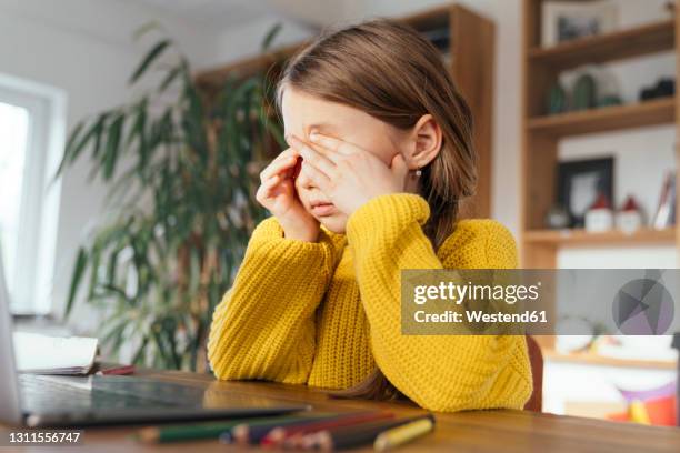 tired girl rubbing eyes while sitting in front of laptop at home - rubbing eyes stock pictures, royalty-free photos & images