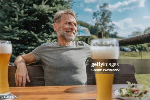 smiling mature man looking away while sitting in beer garden - wheat beer stock pictures, royalty-free photos & images