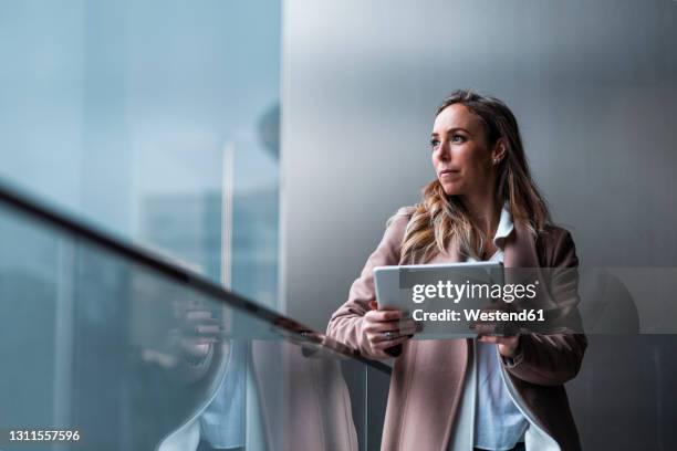 female entrepreneur day dreaming while holding digital tablet in front of gray wall - grey overcoat stock pictures, royalty-free photos & images