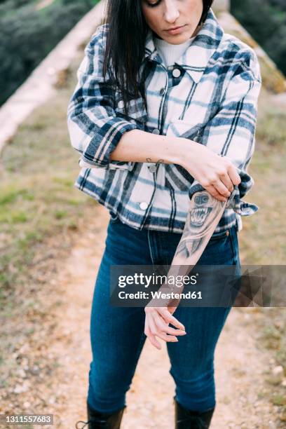 mid adult woman with tattoo rolling up sleeves - rolled up sleeves 個照片及圖片檔