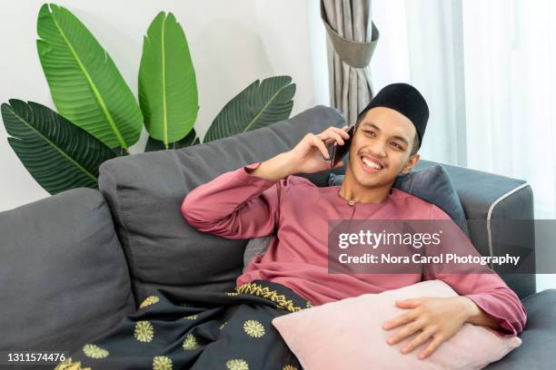 young man with baju melayu talking on the phone - baju melayu stock pictures, royalty-free photos & images