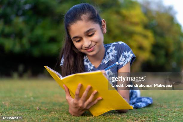 gelukkig laat tiener indisch meisje dat vooraan op gras in park legt en op het notitieboekje schrijft. - 13 pencils stockfoto's en -beelden