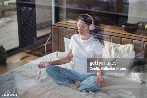 woman sitting on bed, doing yoga. shot through glass. - gefotografeerd door het raam stockfoto's en -beelden