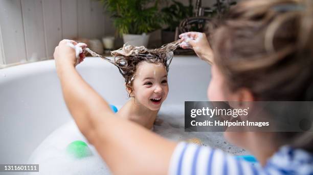 mother with small daughter in bathroom at home, having fun in bath. - kid bath mother stock-fotos und bilder