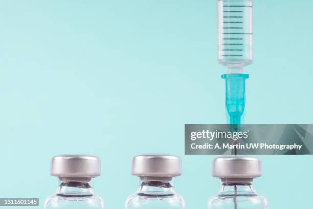 row of medical vials and syringe. glass bottles with a transparent potion on a light background - vaccine fotografías e imágenes de stock