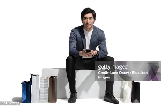 mid adult man using smart phone while sitting with shopping bags - menswear stock pictures, royalty-free photos & images