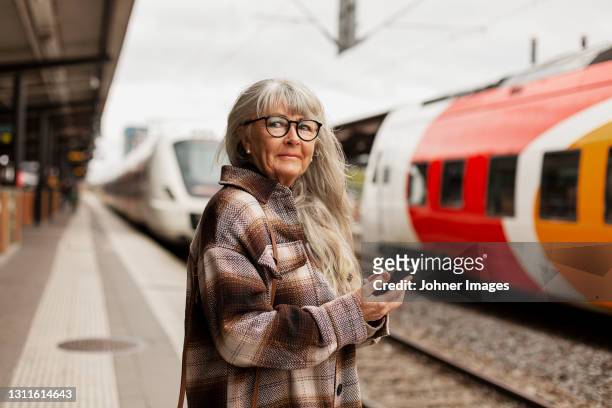 mature woman at train station - frau zug stock-fotos und bilder