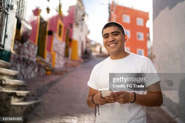 porträt eines jungen mannes mit smartphone auf der straße - mexikanischer abstammung stock-fotos und bilder