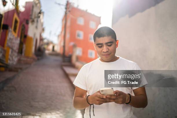 young man texting on smartphone on the street - mexico slums stock pictures, royalty-free photos & images