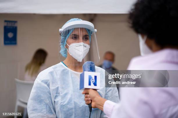 newscaster interviewing a healthcare worker working at a covid-19 vaccination stand - science journalism stock pictures, royalty-free photos & images