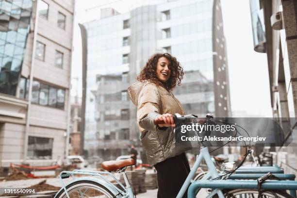 happy curly bicicletta da parcheggio femminile su rack nel centro della città - giacca foto e immagini stock