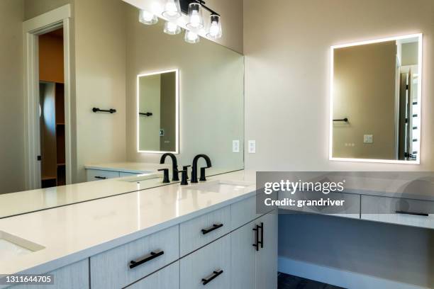 baño de estilo contemporáneo bien iluminado con lavabos, gabinetes y espejo de tocador iluminado - bathroom vanity fotografías e imágenes de stock