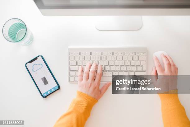 top view of an unrecognizable caucasian woman working in the office while using her mobile phone to download files from the cloud. - bluetooth stock-fotos und bilder