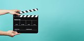 Hand is holding Black clapper board or movie slate on green or mint or Tiffany Blue background.