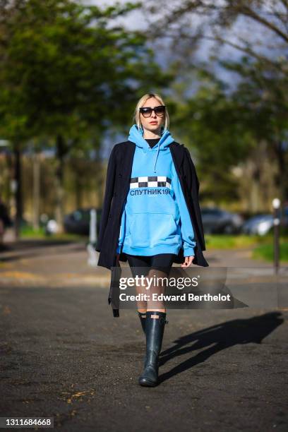 Emy Venturini @sustainably_by_emy wears sunglasses from Dita, a blue hoodie sweater with printed black and white checked logo and Russian words from...