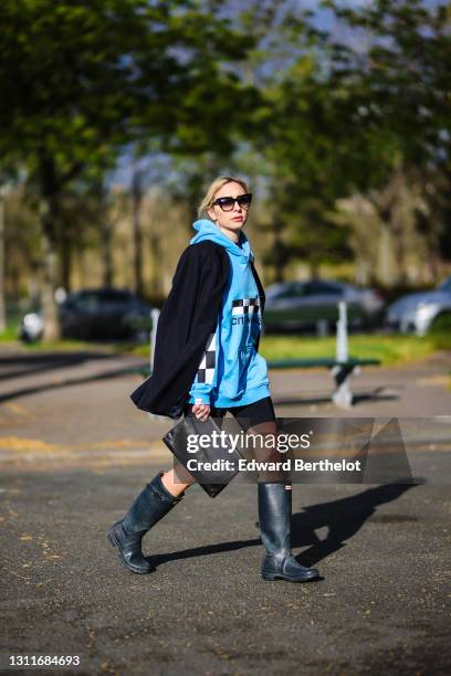 Emy Venturini @sustainably_by_emy wears sunglasses from Dita, a blue hoodie sweater with printed black and white checked logo and Russian words from...