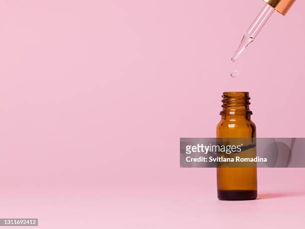 glass brown bottle for cosmetics with pipette. drop of liquid. pastel pink background - ピペット ストックフォトと画像