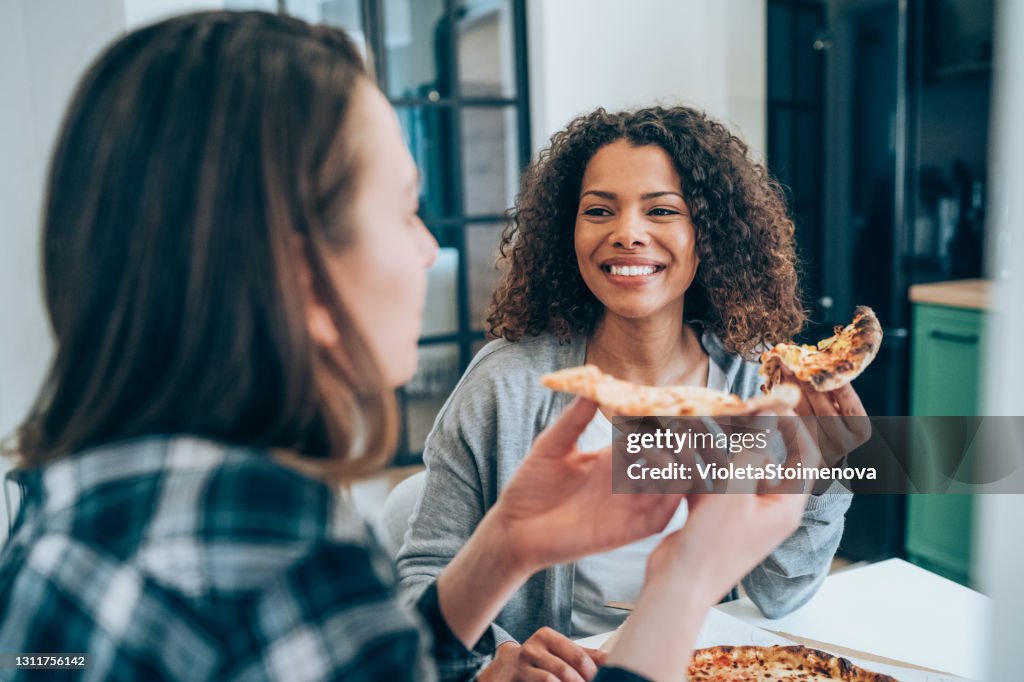 Zwei junge Frauen essen gemeinsam Pizza zu Hause.