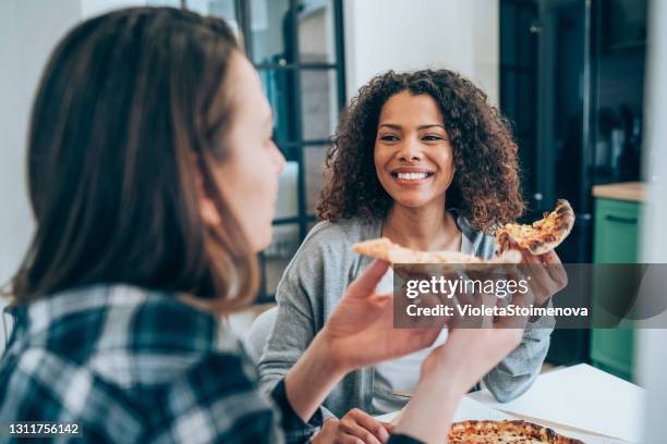 two young women eating pizza together at home. - comer pizza imagens e fotografias de stock