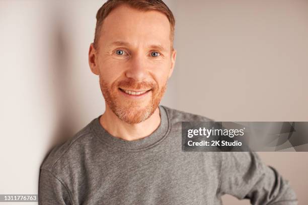 porträtfotos eines mannes in den vierziger jahren mit natürlich roten haaren und bart, bekleidet mit einem grauen langarmhemd, fotografiert im studio vor einem braunen, warmgrauen hintergrund - 2k resolution stock-fotos und bilder