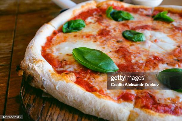 circle pizza margarita with mozzarella and basil leaves on a wooden stand or cutting board, on the table in a cafe or fast food restaurant. traditional italian cuisine. vegetarian food. - pizza crust stock pictures, royalty-free photos & images