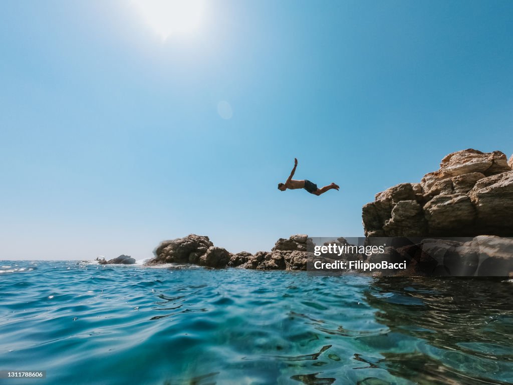 Millennial man is diving from a rock in the sea