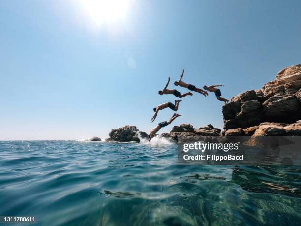 millennial man is diving from a rock in the sea - multiple images effect - cliff stock pictures, royalty-free photos & images