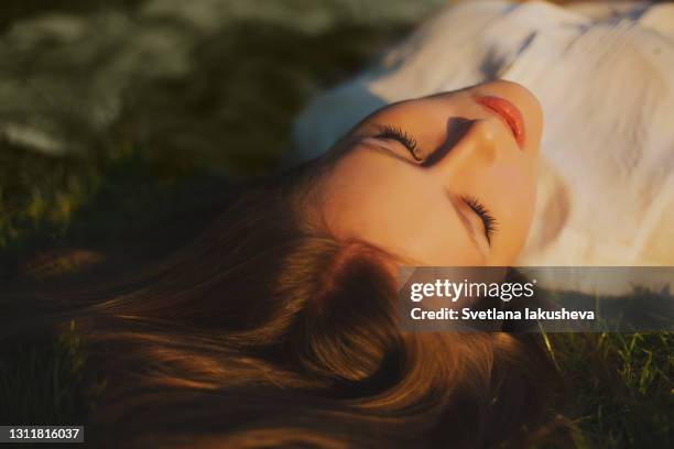 a young girl lies on the grass in the park, resting, basking in the sun and enjoying the sunset - long eyelashes stock pictures, royalty-free photos & images