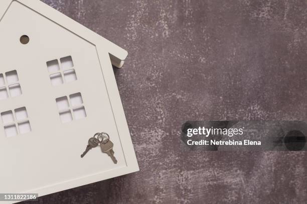 a toy wooden white house on a gray background, on the house are metal keys. the concept of a real estate purchase offer. copy the space. mortgages, affordable housing. - viviendas asequibles fotografías e imágenes de stock