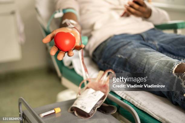 spender drückt den herzförmigen ball während der blutspende - donation stock-fotos und bilder