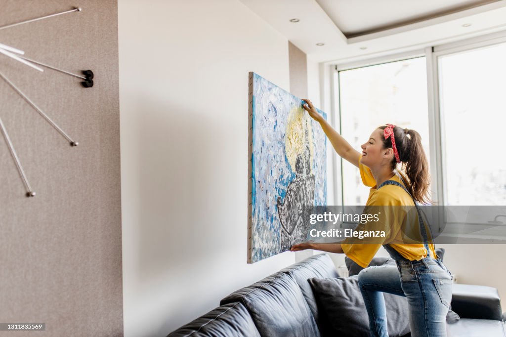Junge Frau hängen Kunstbild an der Wand und dekorieren Wohnzimmer