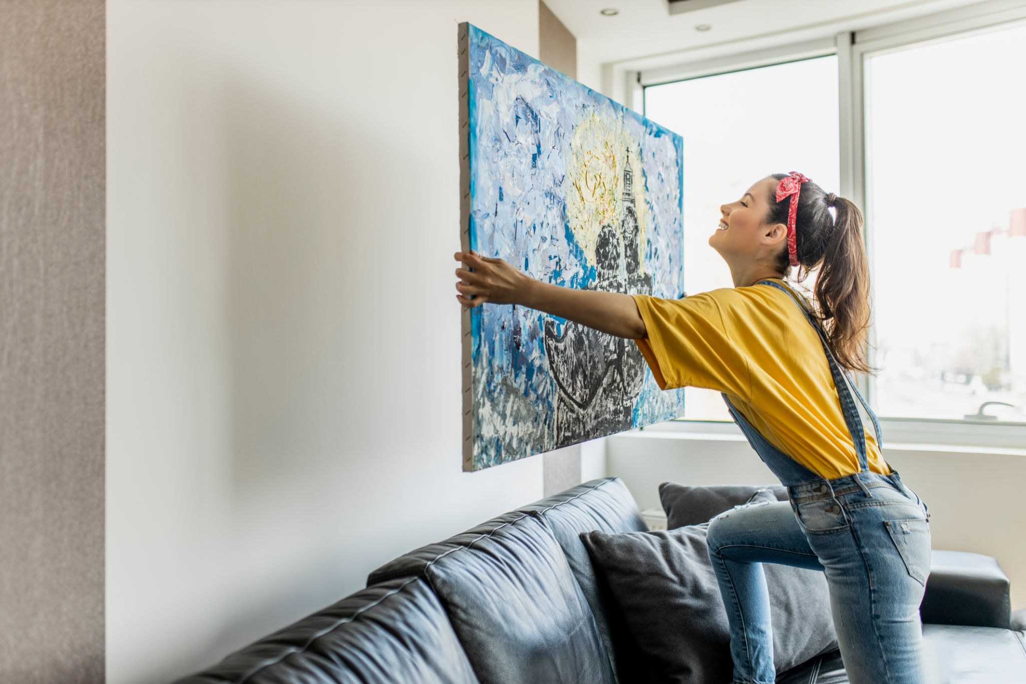 Young woman hanging art picture on wall and decorating living room Young woman hanging art picture on wall and decorating living room