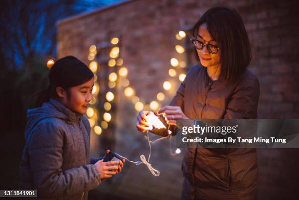 mom & daughter untangling the string lights together while they are decorating the garden at dusk - hanging in garden photos et images de collection