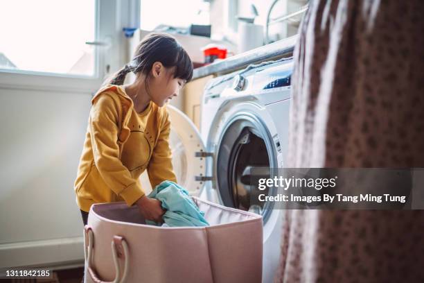 lovely little girl unloading the washing machine while helping her mom with laundry at home - lessive corvée domestique photos et images de collection