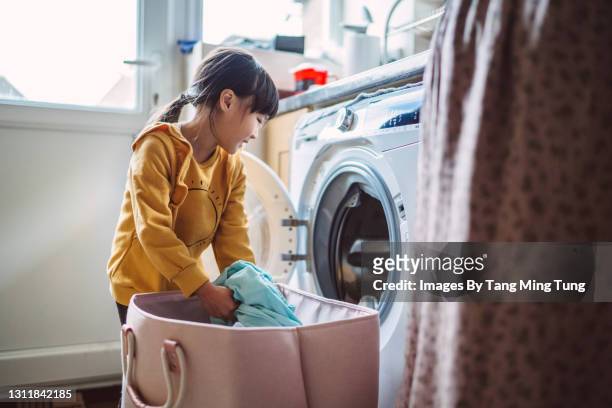 lovely little girl unloading the washing machine while helping her mom with laundry at home - asian young family stockfoto's en -beelden