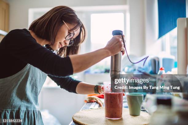 young pretty woman making fruit smoothie at home - mixer stock-fotos und bilder