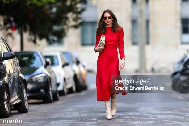 Therese Hellström wears sunglasses, a red midi long dress with sleeves, a Chanel bag, beige square toe high heels shiny boots, on April 08, 2021 in...