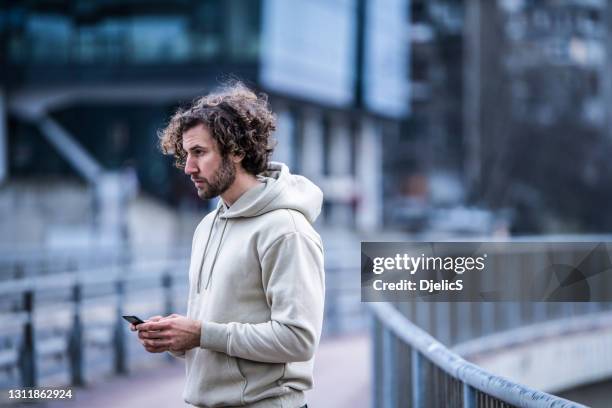 junger mann mit telefon in der stadt. - sweatshirt stock-fotos und bilder