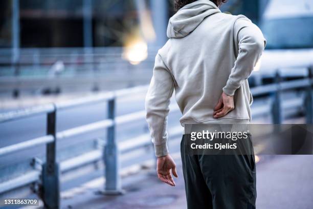 joven atleta masculino que tiene un dolor de espalda. - injured street fotografías e imágenes de stock