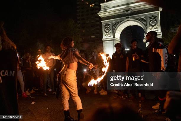Woman without a mask performs tricks with fire as people gather around to watch in Washington Square Park amid the coronavirus pandemic on April 10,...