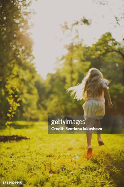 a school-age girl with blond hair in a white dress in a summer park in the sunset rays runs - red dress run stock pictures, royalty-free photos & images