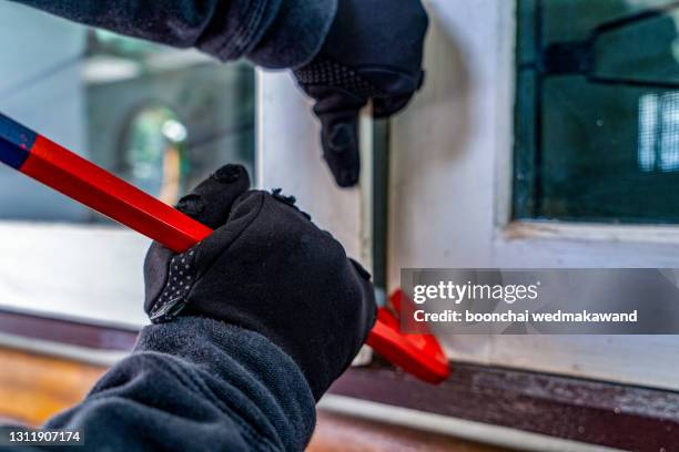 close-up of robber in hood using the red crowbar to open the glass window - einbruch stock-fotos und bilder