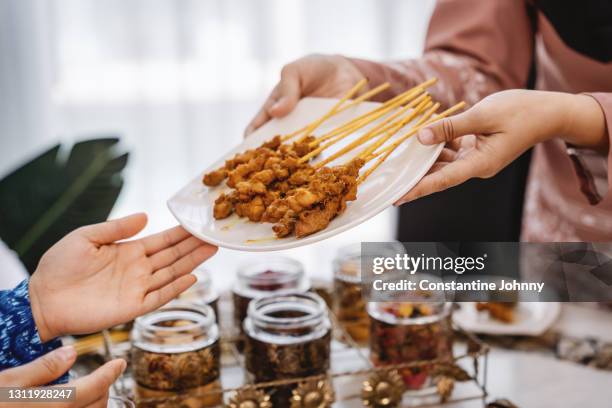 close up of hands holding and sharing chicken satay on plate with friends - chicken satay stock-fotos und bilder