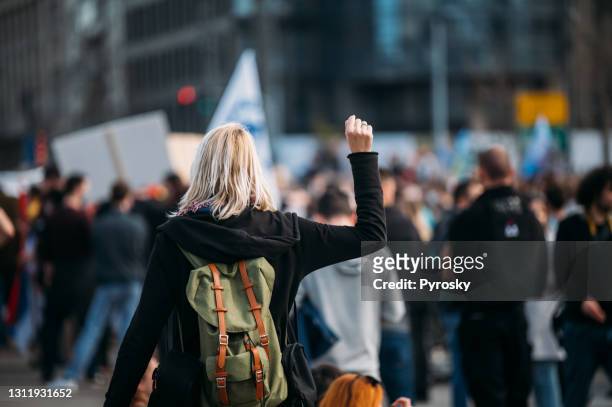 achter mening van een vrouwelijke demonstrant die haar vuist omhoog optilt - demonstration stockfoto's en -beelden