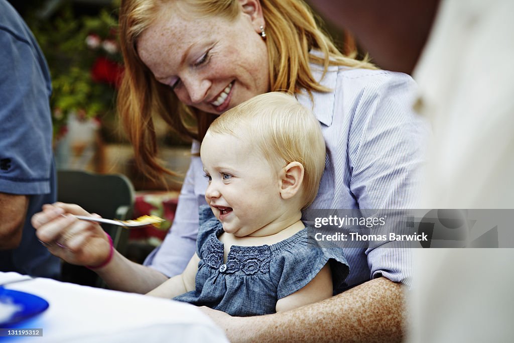 Mother feeding baby daughter at table outside