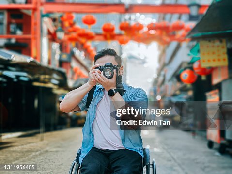 asian chinese male with physical disability on wheelchair photographing in china town sitting on his wheelchair