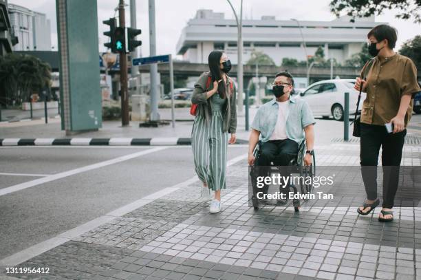 asian chinese male with disability on wheelchair crossing road with his friends in kuala lumpur - kuala lumpur road stock pictures, royalty-free photos & images