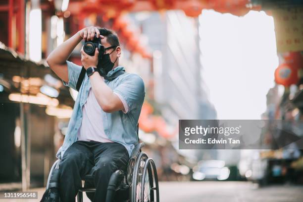 asian chinese male with physical disability on wheelchair photographing in china town sitting on his wheelchair - asian journalist stock pictures, royalty-free photos & images