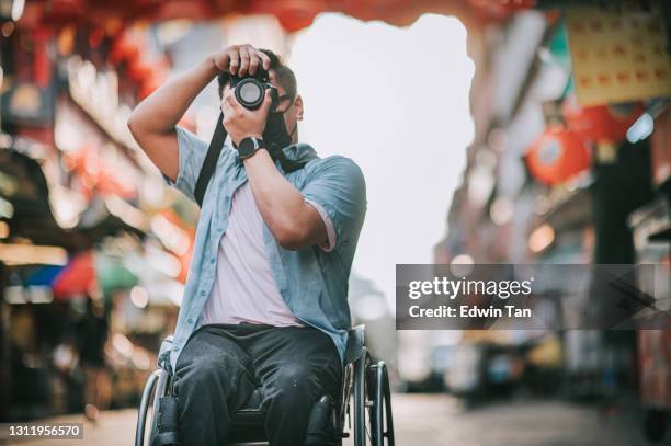 asiatische chinesische männlich mit körperlicher behinderung auf rollstuhl fotografieren in china stadt sitzend auf seinem rollstuhl - man wheel chair stock-fotos und bilder